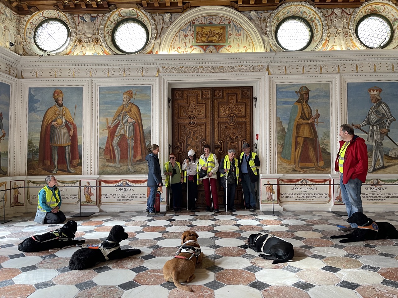 Weiterbildung im Spanischen Saal in Schloss Ambras. In einem prunkvollen Saal stehen mehrere Sehbeinträchtigte Menschen  ihren brav wartenden Hunden gegenüber.